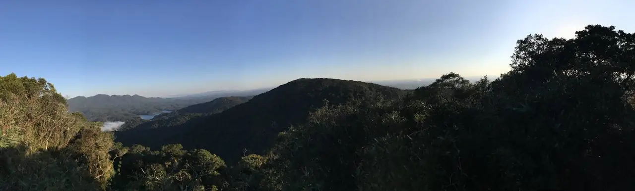 Panorama da serra coberta de mata, com uma represa ao fundo