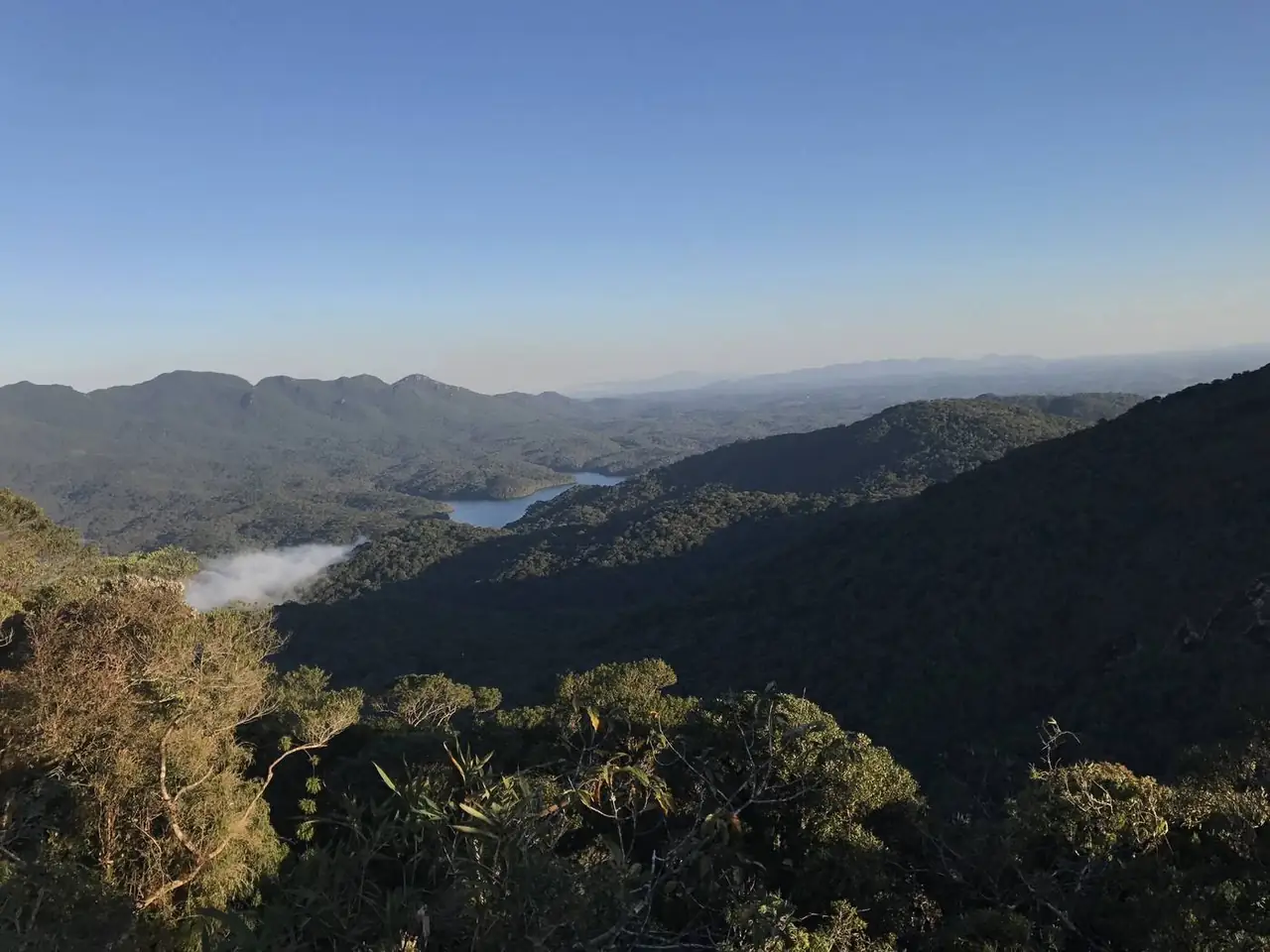 Vale com uma represa e serras ao fundo, visto do alto